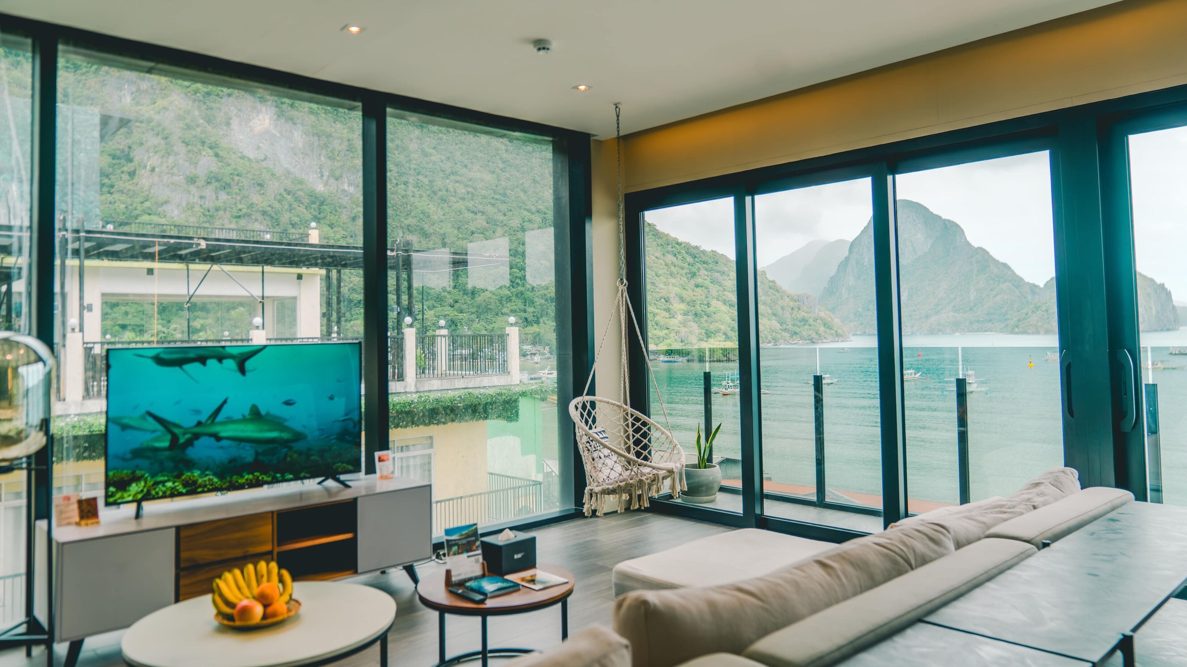 A modern living room with a large TV, a sofa, a small table with fruit, and a chair.