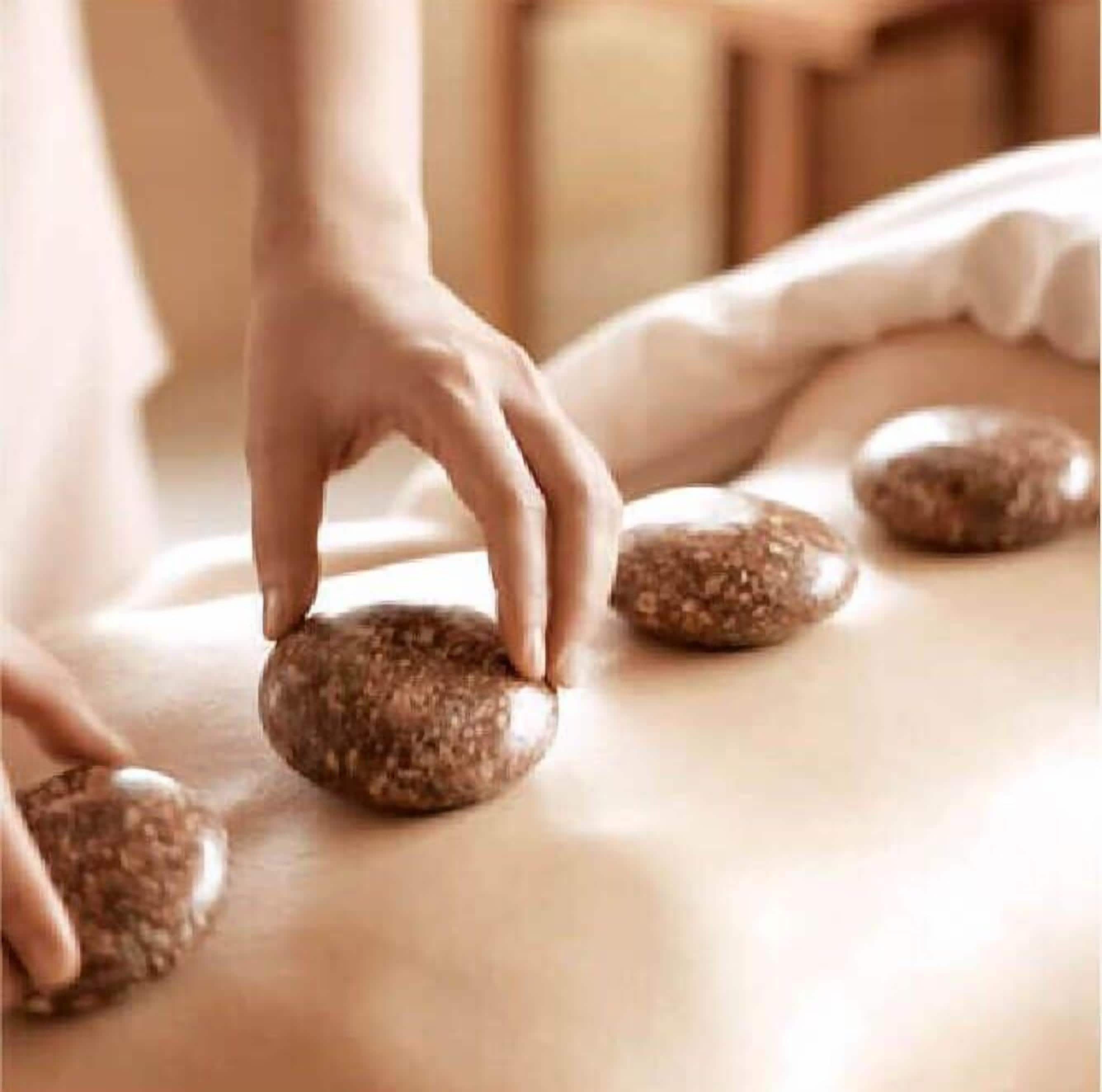 A person placing a stone on a massage table.