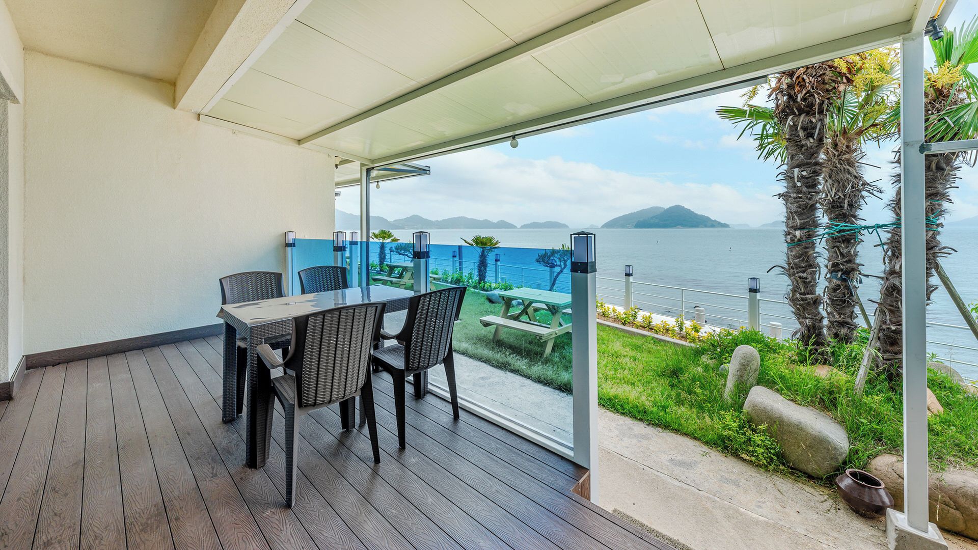 A covered outdoor seating area with a table and chairs, overlooking a body of water and a distant island.