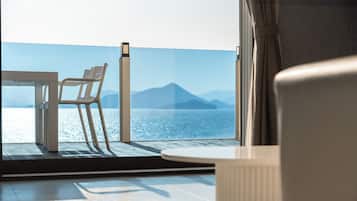 Un balcón con mesa y sillas, con vista a un cuerpo de agua y montañas a lo lejos.