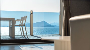 A balcony with a table and chairs, overlooking a body of water and distant mountains.