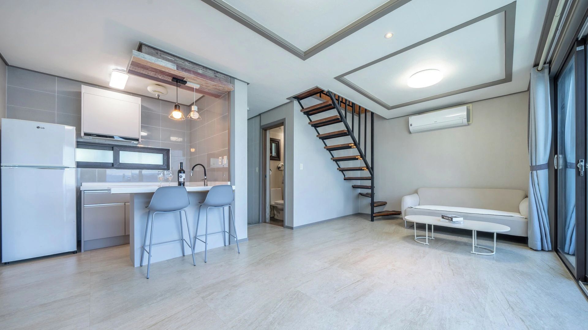 Una cocina moderna con refrigerador integrado, taburetes de bar e iluminación colgante.