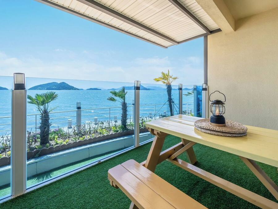 A balcony with a wooden table and bench, overlooking a body of water and distant islands.