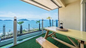A balcony with a wooden table and bench, overlooking a body of water and distant islands.