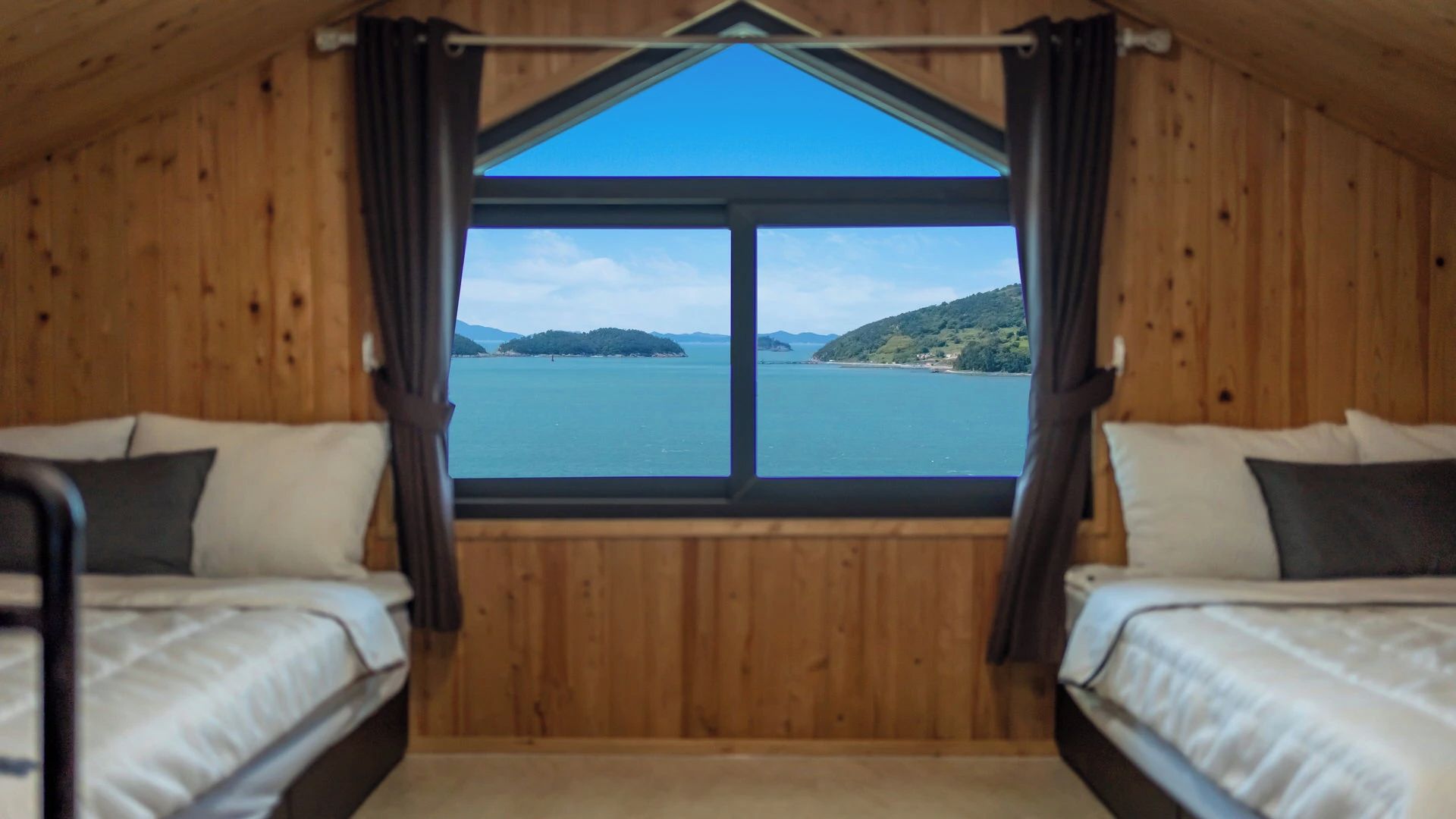 Una cabaña con dos camas, un ventanal grande y vistas al agua y colinas.