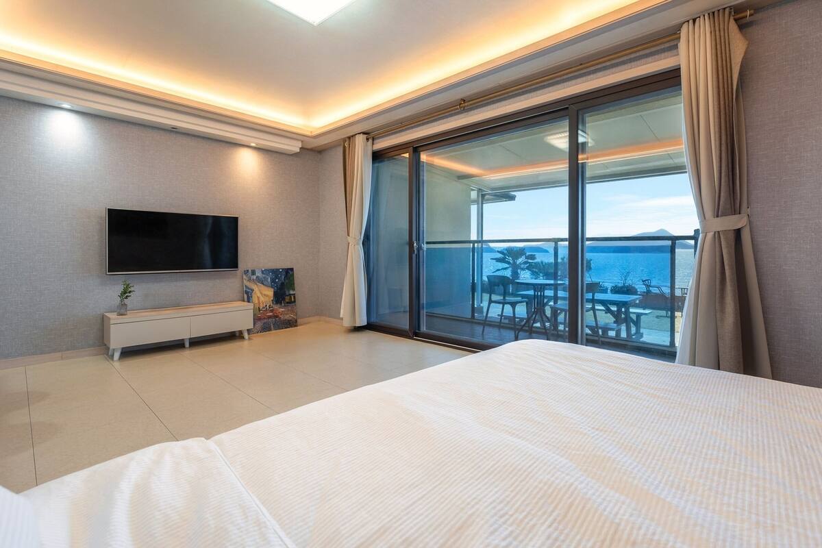 Ett modernt hotellrum med en stor säng, en platt-TV, en tavla och en balkong med utsikt över havet.