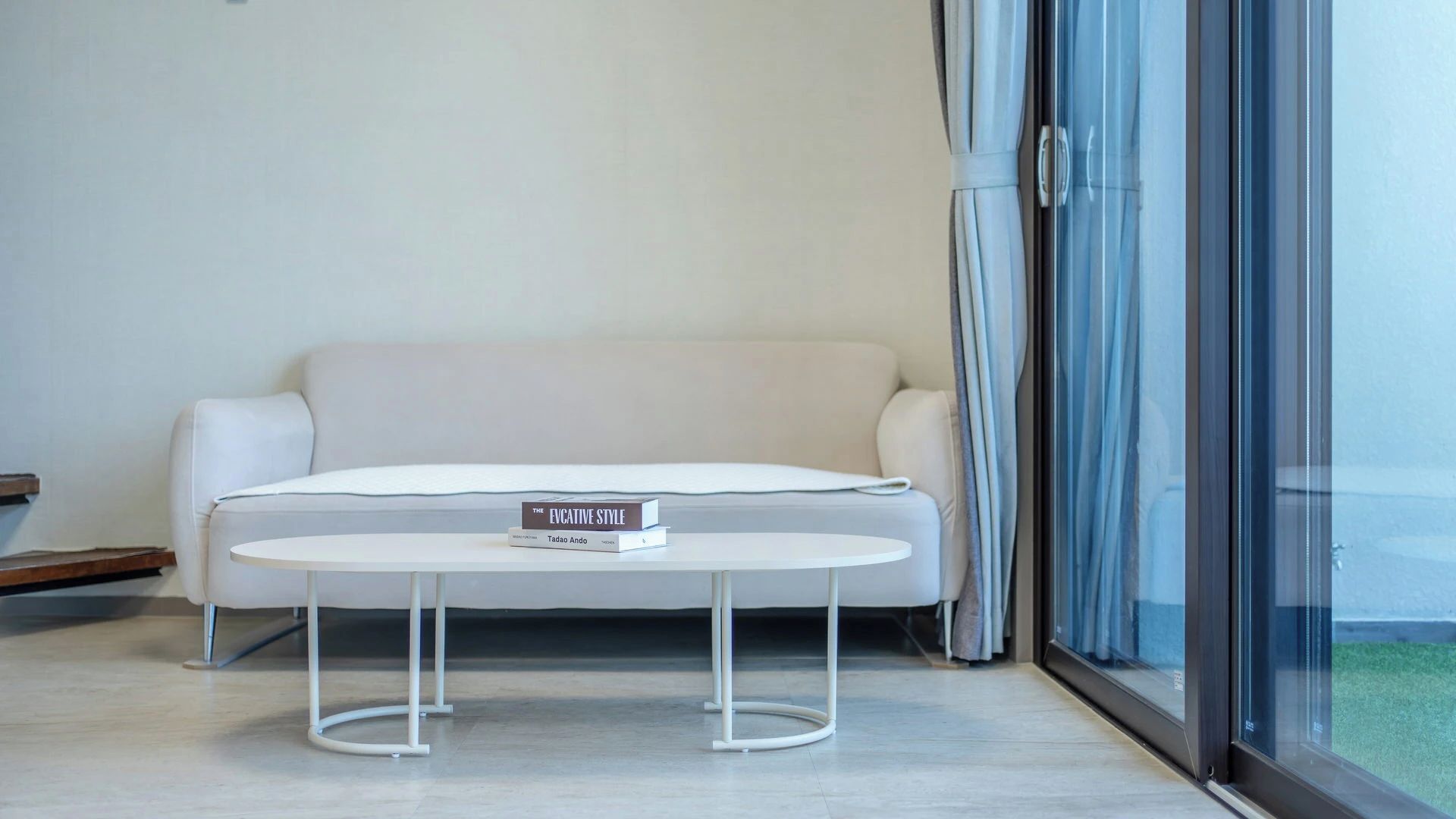 A modern living room with a white sofa, a round coffee table, and a large window with curtains.