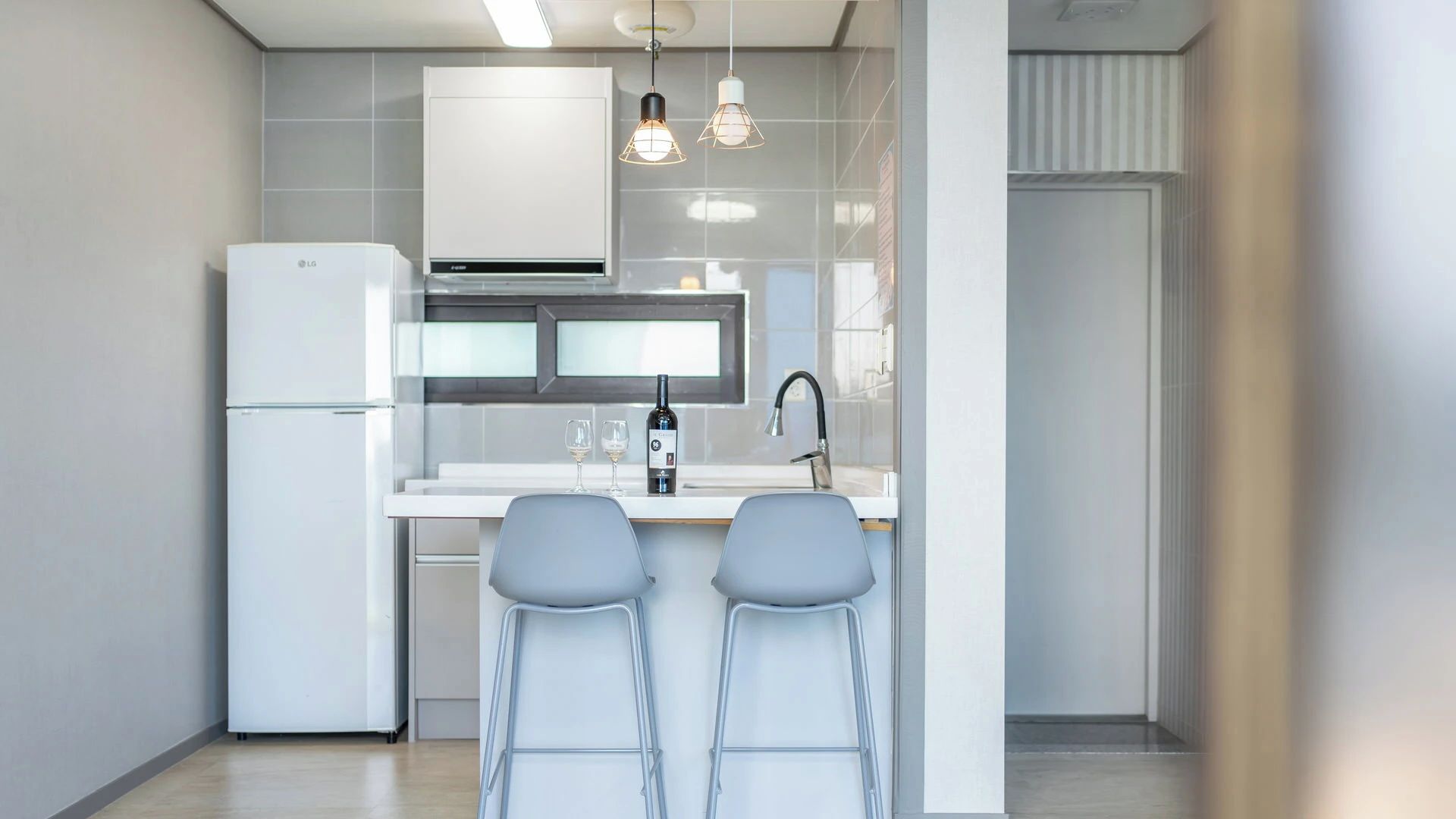 Une cuisine moderne avec un réfrigérateur blanc, un four encastré, un évier en acier inoxydable et deux tabourets de bar.