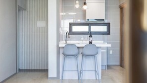 A modern kitchen with a built-in TV, two bar stools, and a wine bottle on the counter. - Yeosu Baraboda Ocean View Pension (Yeosu)