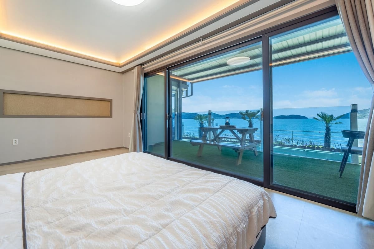 Ett hotellrum med en stor säng, ett skrivbord och utsikt över havet genom en skjutdörr av glas.