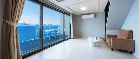 A modern hotel room with a large sliding glass door leading to a balcony with a view of the sea and mountains.