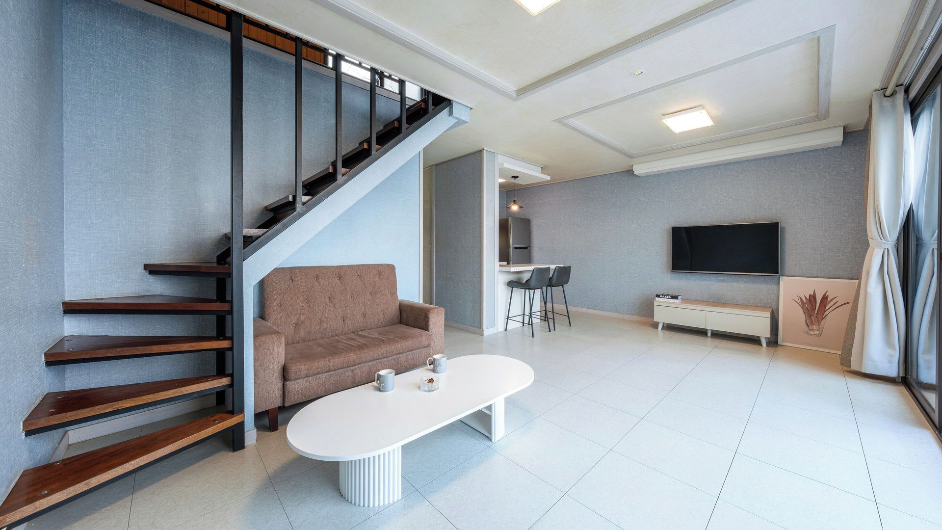 Una sala de estar moderna con una escalera, un sofá, una mesa de centro, un televisor y una zona de cocina.