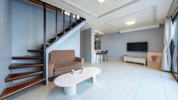 Una sala de estar moderna con una escalera, un sofá, una mesa de centro, un televisor y una zona de cocina.