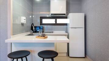 A compact kitchen with a white refrigerator, a sink with a modern faucet, and a window above the counter.