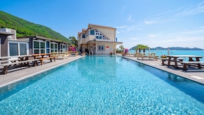 A swimming pool with a view of the sea, a building with a balcony, and outdoor seating. - Yeosu Baraboda Ocean View Pension (Yeosu)
