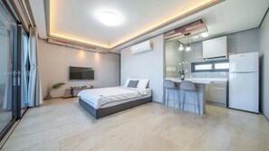 A modern bedroom with a large bed, a TV, and a kitchenette with a fridge.