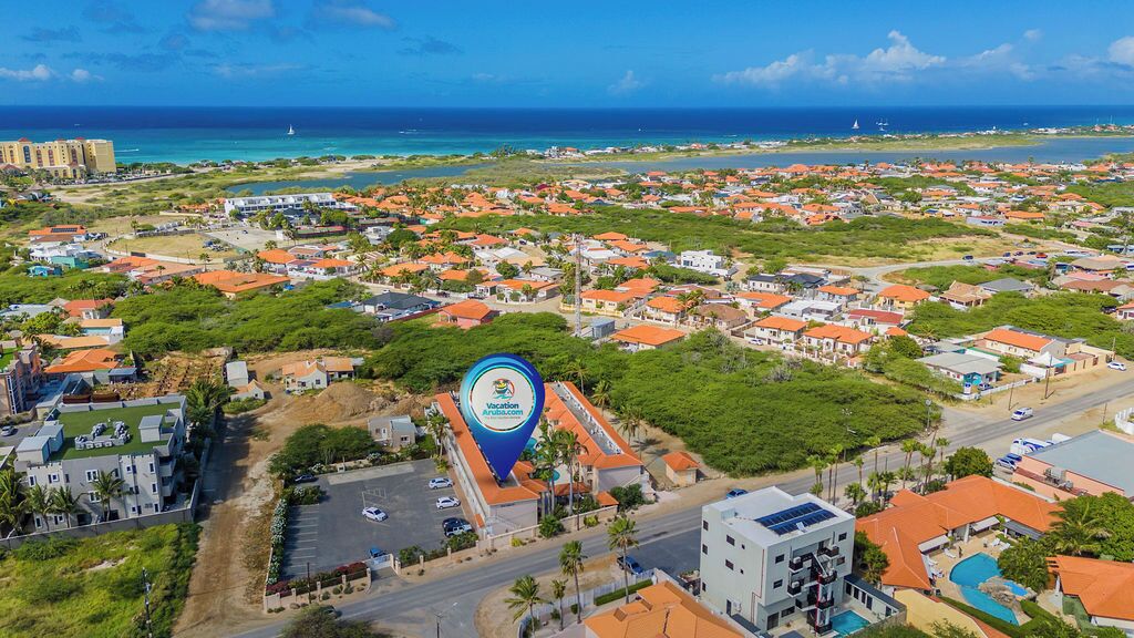 A coastal town with a prominent hotel featuring a large blue sign, surrounded by residential buildings and a clear view of the ocean.