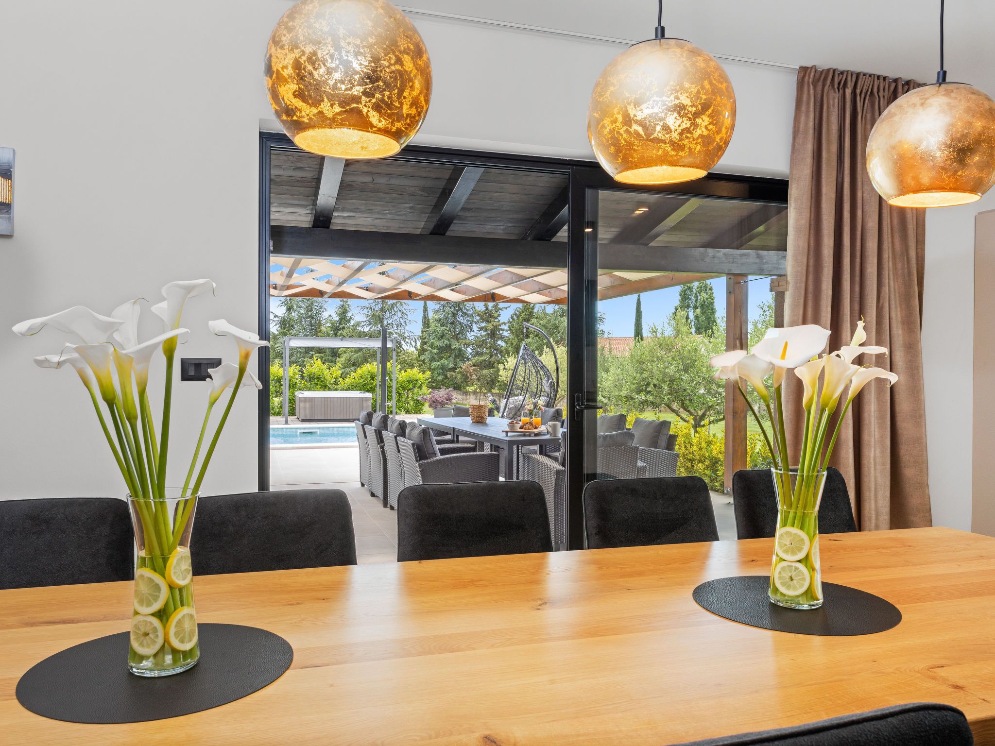 Un espace repas avec une table en bois, deux vases ornés de fleurs blanches et des luminaires sphériques suspendus au plafond.