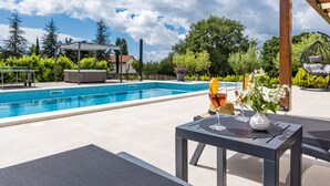A poolside area with a clear view of the pool, a covered seating area, and a table with a drink and flowers. - Villa Venezia by Interhome (Labin)