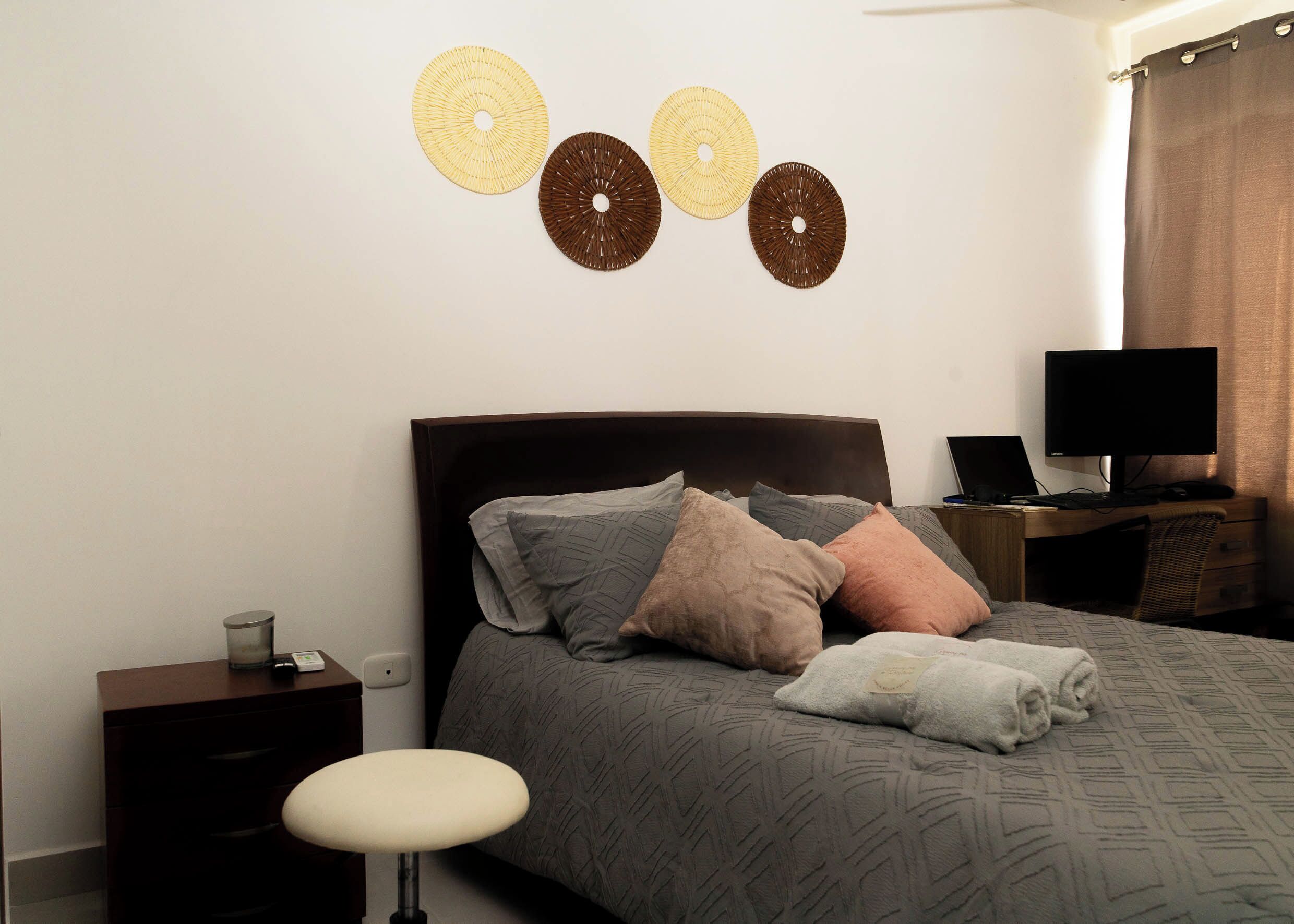 Ein ordentlich eingerichtetes Schlafzimmer mit Bett, Nachttisch, Lampe und Schreibtisch mit Computer.