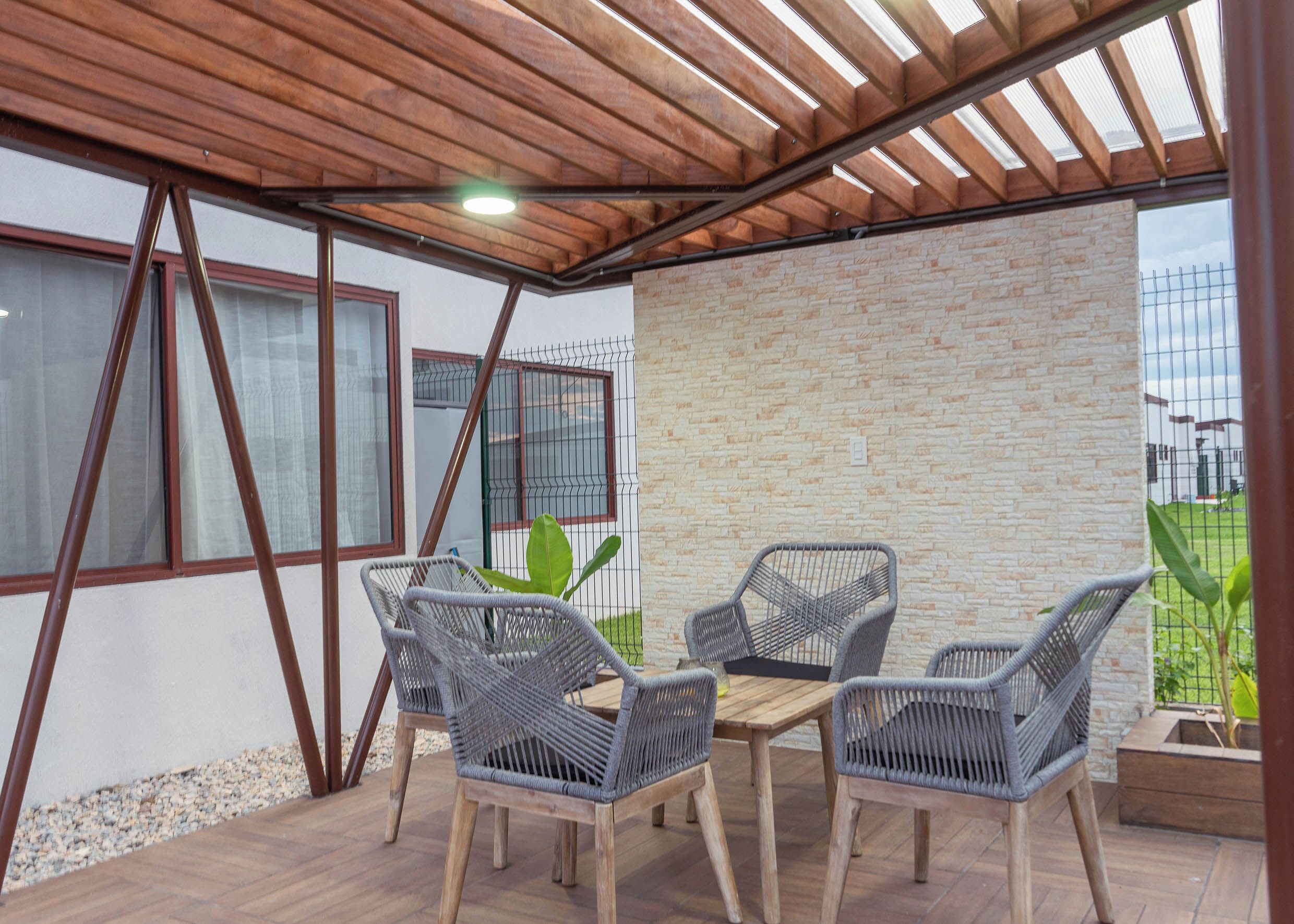 Een overdekt terras met een houten plafond, een bakstenen muur en een tafel met vier rieten stoelen.