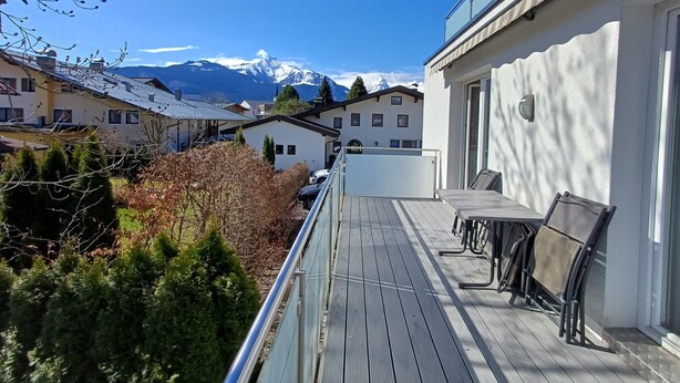 A balcony with a table and chairs, overlooking a mountain range and neighboring buildings.