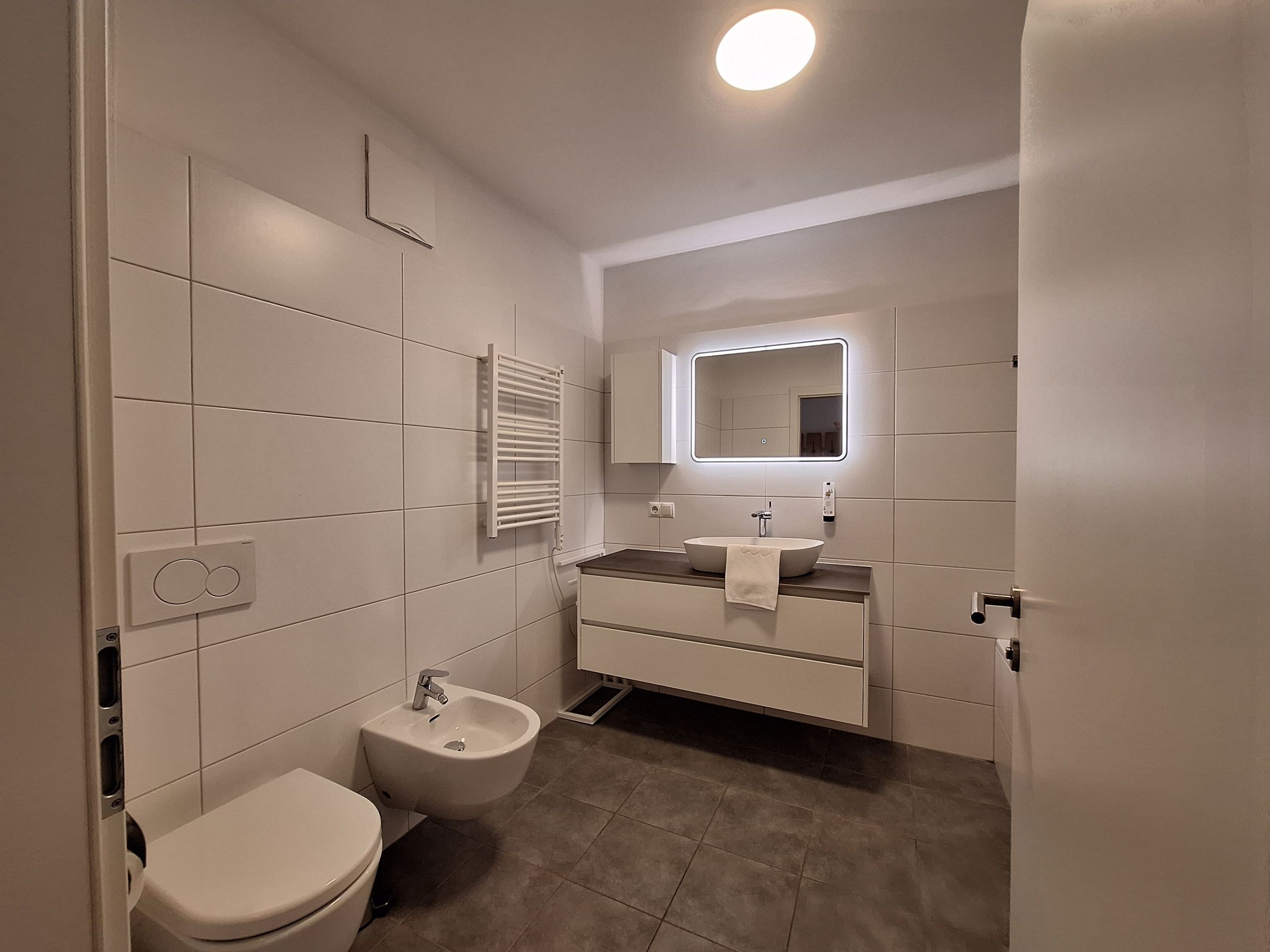 A modern bathroom with a toilet, bidet, vanity with a mirror, and a towel rack.