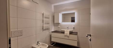 A modern bathroom with a toilet, bidet, vanity with a mirror, and a towel rack.