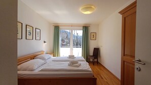 A bedroom with a wooden bed, a chair, a door, and a window with curtains.