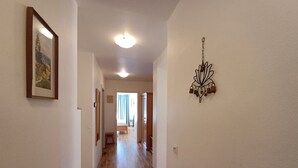 A hallway with wooden flooring, a framed picture on the left, and a wall-mounted light fixture on the right.
