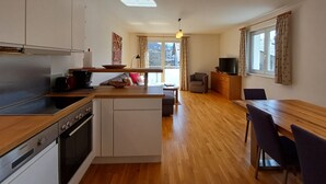 A modern kitchen with a Siemens oven, a dining area with a wooden table and chairs, and a view of the outside through large windows.