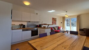 A modern kitchen with white cabinets, a wooden dining table, and a large window with curtains.
