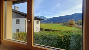 Una habitación con un gran ventanal que ofrece vistas a una casa, un campo verde y montañas.