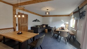 Una sala de estar moderna con una mesa de comedor de madera, un sofá y un televisor montado en la pared.