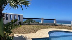 Une piscine offrant une vue dégagée sur l’océan et un bâtiment blanc doté de fenêtres en arc de cercle.