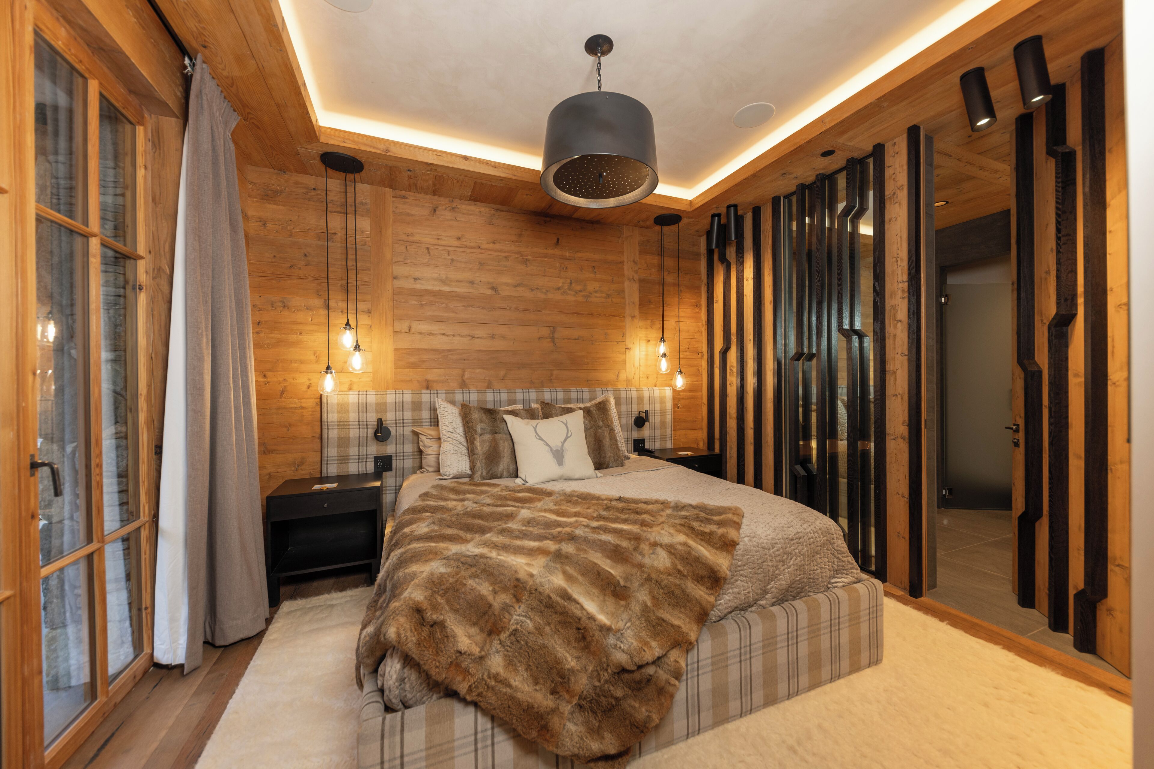 A bedroom with a large bed, wooden walls, a ceiling light, and a nightstand.