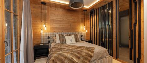 A bedroom with a large bed, wooden walls, a ceiling light, and a nightstand.