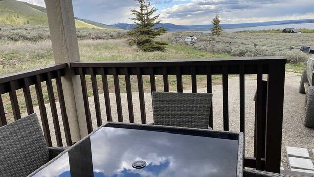 Een terras buiten met een tafel en stoelen, met uitzicht op een gazon met bomen en verre bergen.