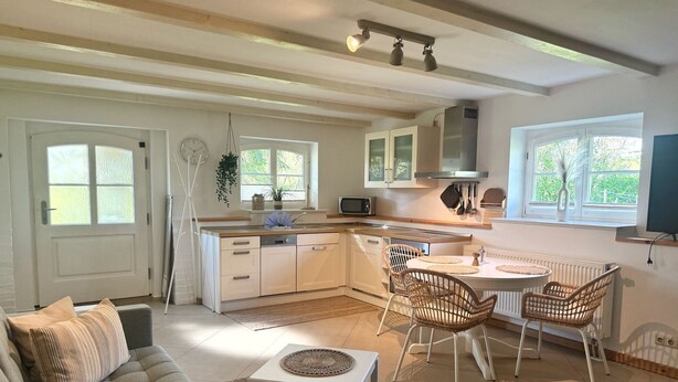 A modern kitchen with white cabinetry, a dining area with wicker chairs, and a sofa with cushions. - Ferienwohnung Alvine - Dubnitz - Doppelhaushälfte Alwine (Sassnitz)