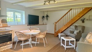 A modern kitchen with a dining area, a TV mounted on the wall, and a wooden staircase. - Ferienwohnung Alvine - Dubnitz - Doppelhaushälfte Alwine (Sassnitz)