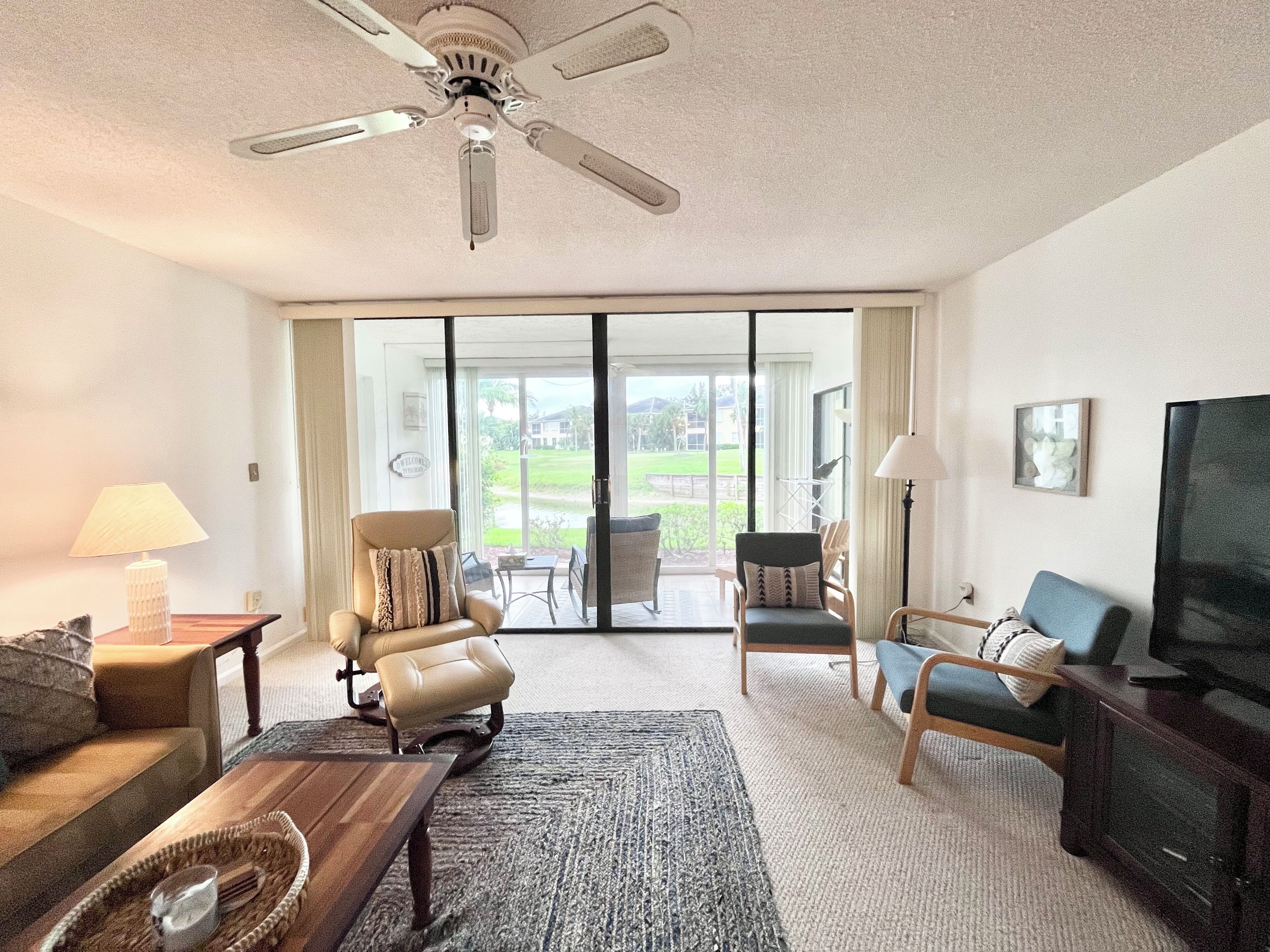 A spacious living room with a ceiling fan, a television, and a view of the outdoors through large sliding glass doors.