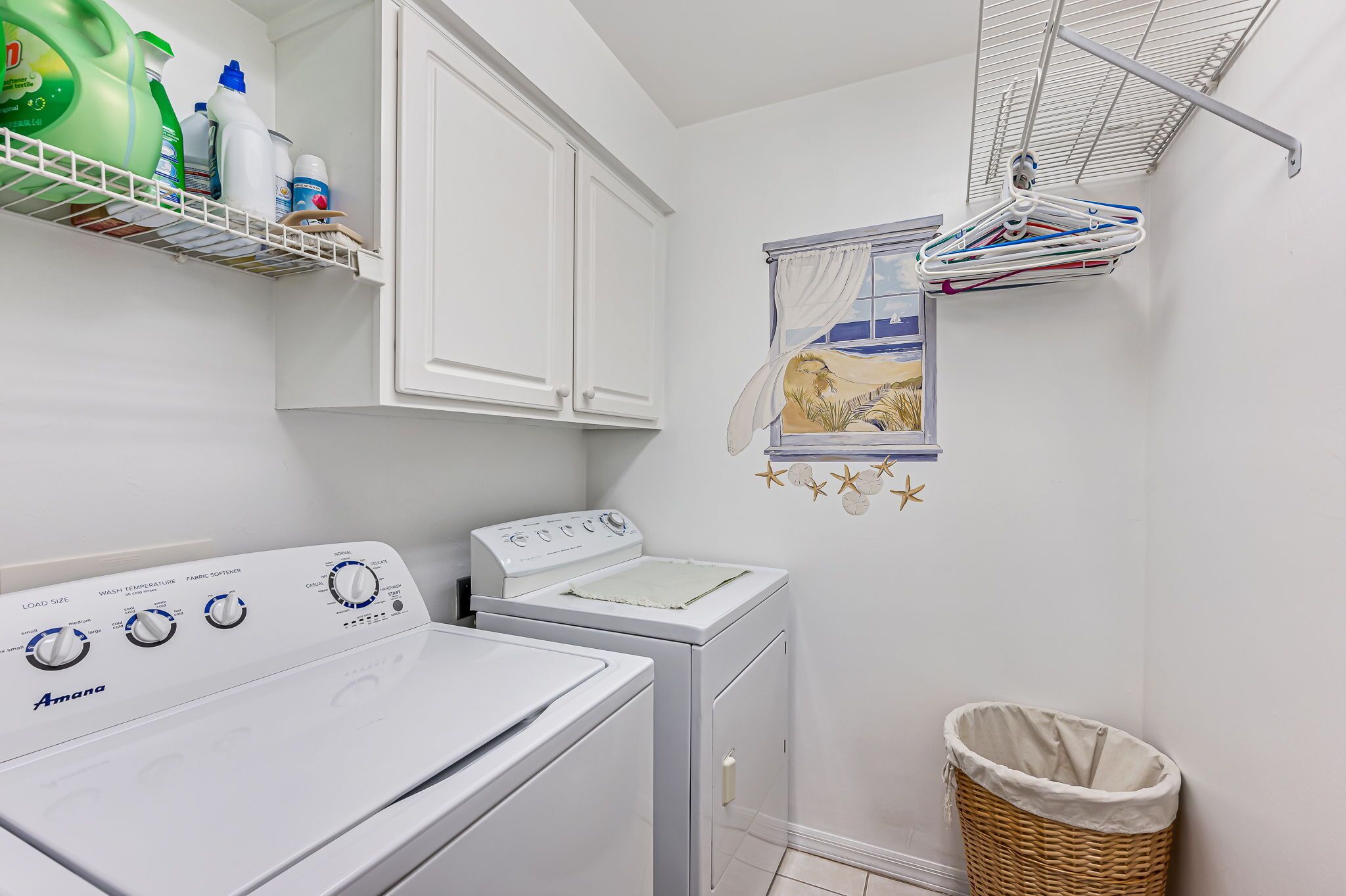 A laundry area with a washer and dryer, a drying rack, and a shelf with cleaning supplies.