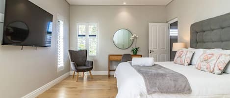 A bedroom with a bed, a desk, a chair, a TV, and a door.