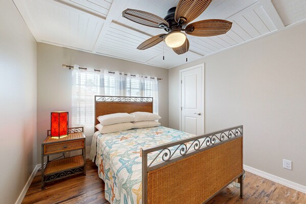A bedroom with a bed, a nightstand, a wall-mounted ceiling fan, and a window with curtains.