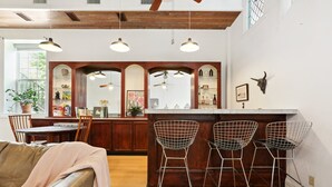 Une cuisine avec des meubles en bois, un coin bar avec des chaises en fil de fer et un coin repas avec un canapé en cuir.