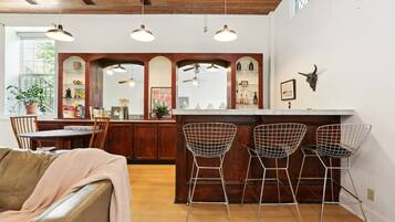 A kitchen with wooden cabinets, a bar area with wire chairs, and a dining area with a leather couch.
