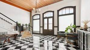 Un hall d’entrée spacieux avec un sol à carreaux, un escalier et un coin salon agrémenté d’une plante.