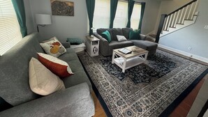 Ein Wohnzimmer mit grauem Sofa, Couchtisch und einem gemusterten Teppich.