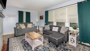 Ein Wohnzimmer mit grauem Sofa, einem Holztisch und einem gemusterten Teppich.