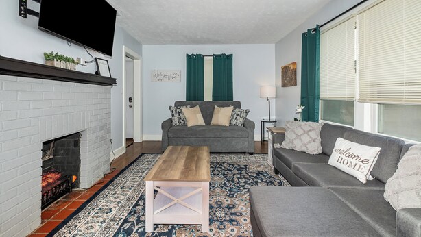 Ein Wohnzimmer mit Kamin, grauen Sofas, einem Couchtisch und einem an der Wand montierten Fernseher.